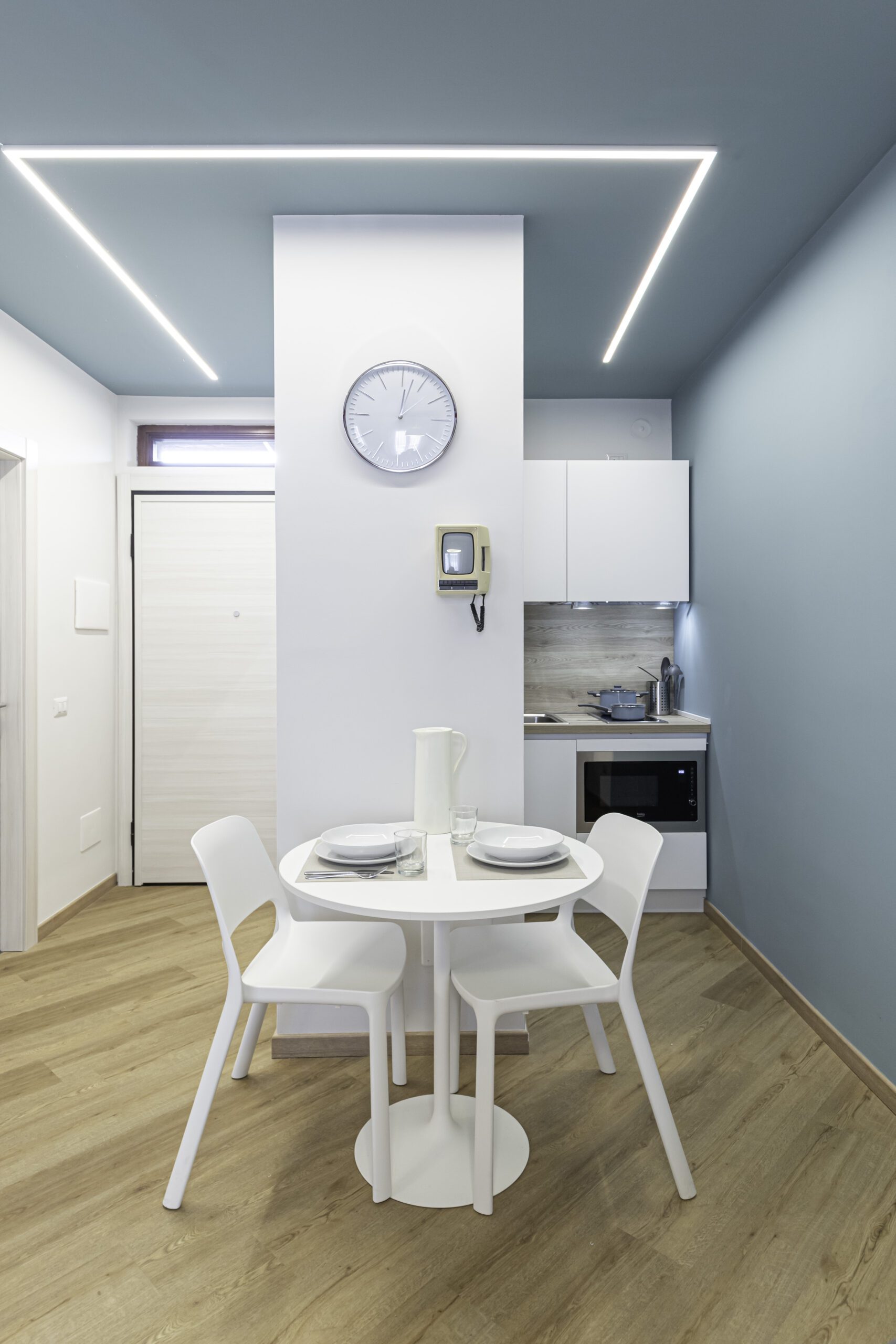 Open space luminoso nei toni dell'azzurro e ottanio, con una piccola cucina bianca integrata e un elegante tavolo da pranzo rotondo