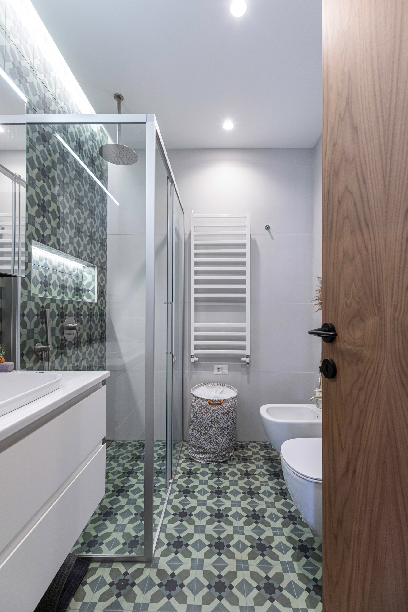 Bagno elegante in verde scuro, con mattonelle geometriche e doccia in cristallo.